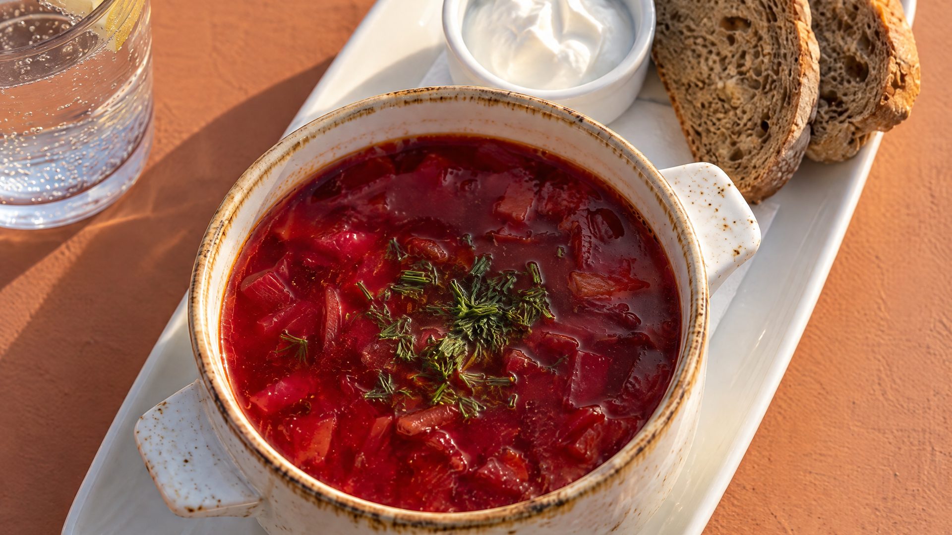 A bowl of beetroot soup with soured cream and rye bread on a terracotta table