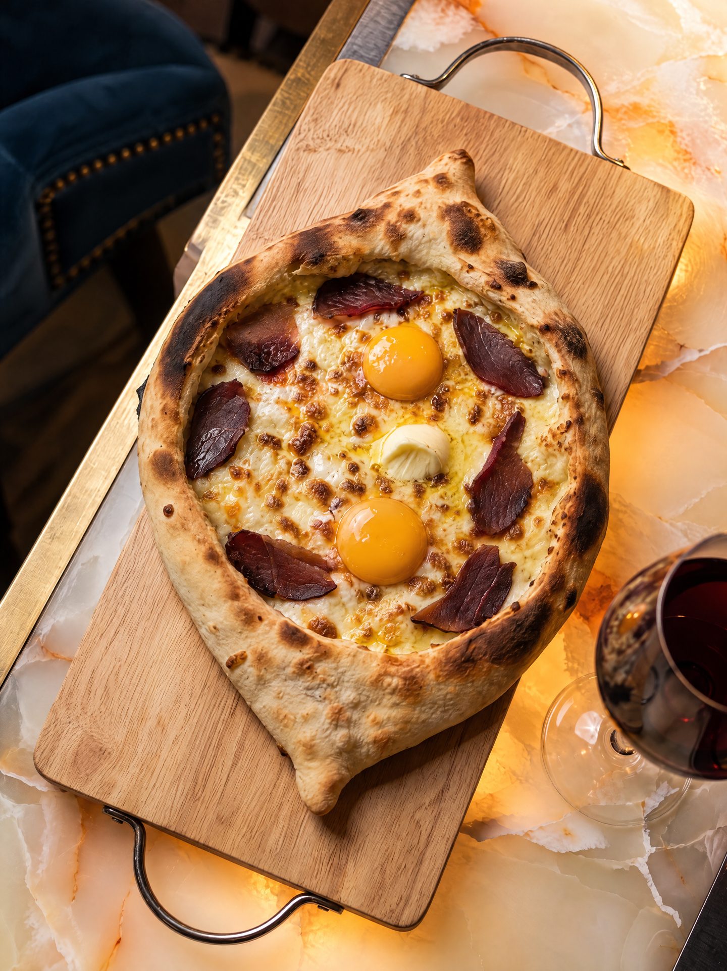 Boat-shaped bread with egg yolks, melted cheese and slices of cured beef on a wooden board