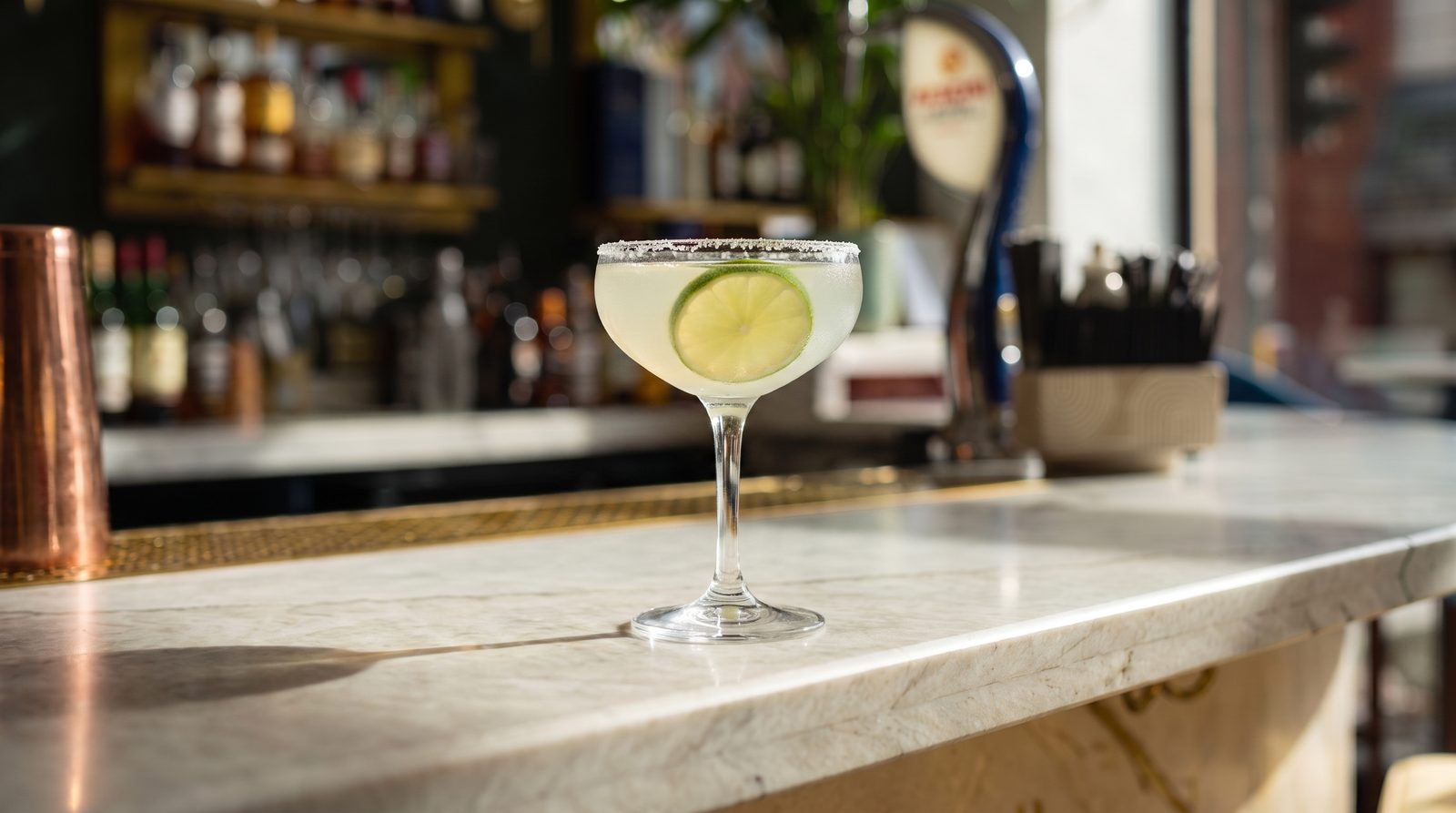 A Margarita with a salted rim and a slice of lime on the marble bar