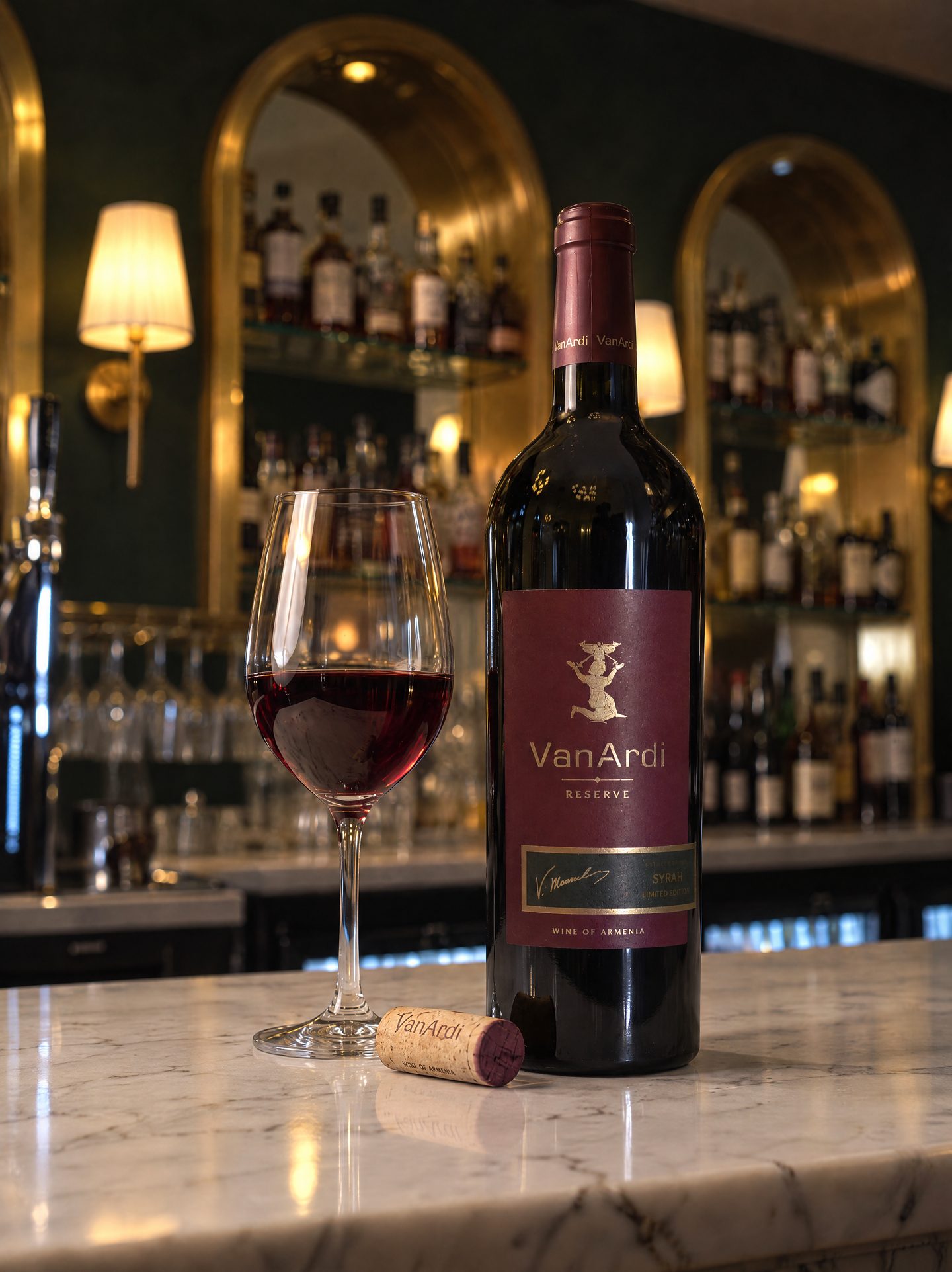 A bottle of Van Ardi Reserve Syrah beside a poured glass of red on the marble bar