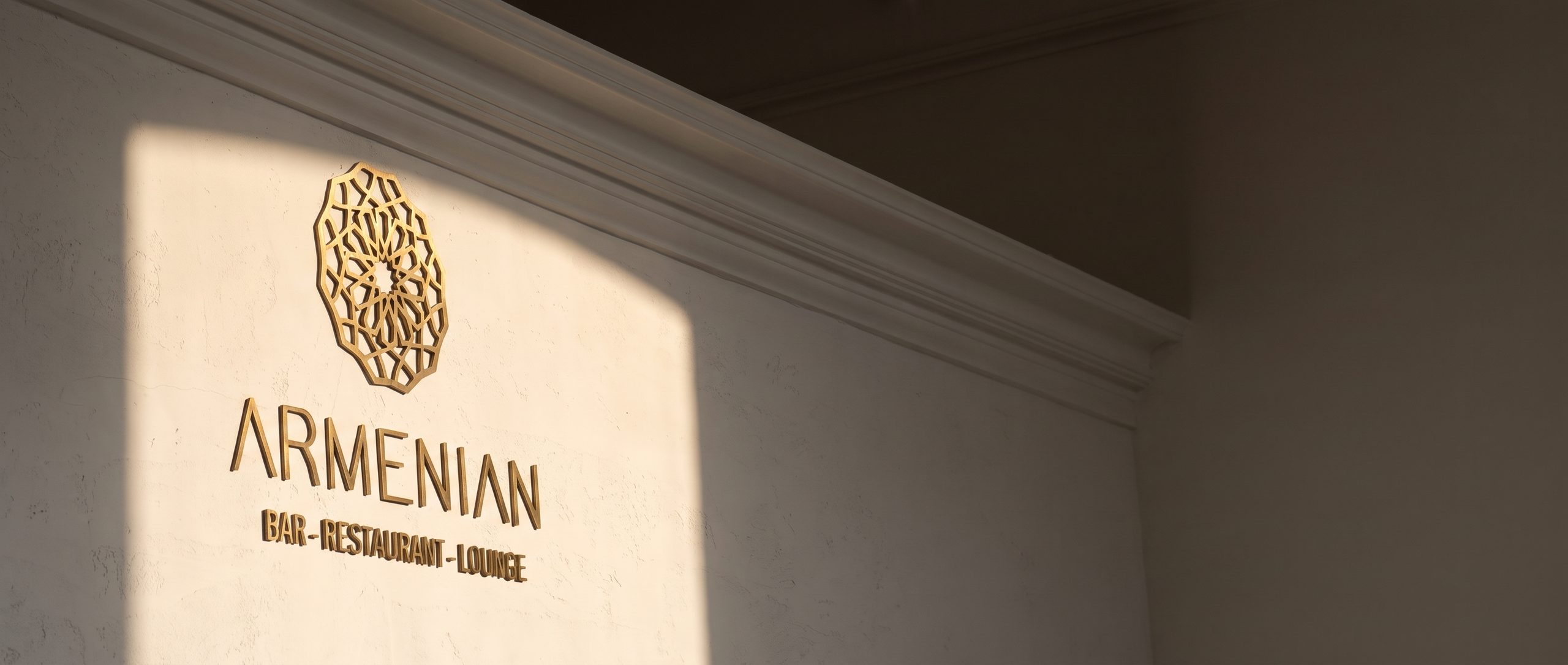 The restaurant's gold rosette and ARMENIAN lettering on a pale wall, lit by a shaft of sunlight